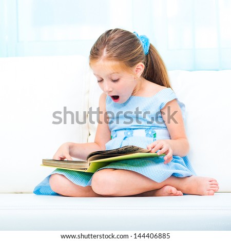 little cute girl reading a book and siting on the sofa