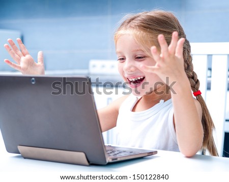 Glad Little Girl With Her Computer At Home At The Table