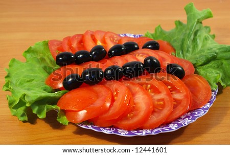 Tomatoes, leaves of salad and olives on a round plate