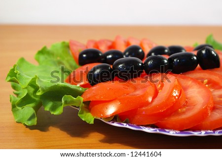 Tomatoes, leaves of salad and olives on a round plate