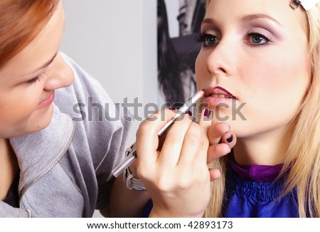 Makeup artist tracing red contour on the lips of a girl