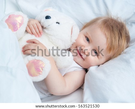 beautiful baby lying in white bed and holding a teddy bear toy