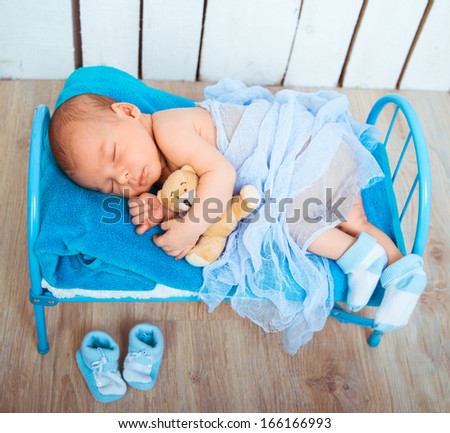 Cute newborn baby sleeps in a small bed with teddy bear