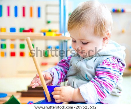 cute little girl in the classroom early development plays with numerous bright toys