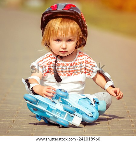 two year old pretty girl in roller skates and a helmet sitting on the street