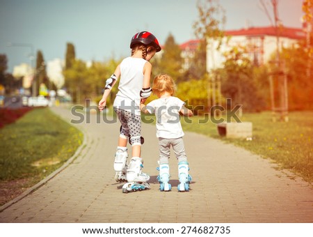 two little sisters to roller skate on the street, back view