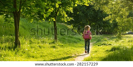 happy little girl go to school through the forest. back view