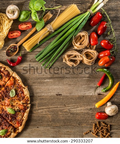 Italian food background with pizza, raw pasta and vegetables on wooden table