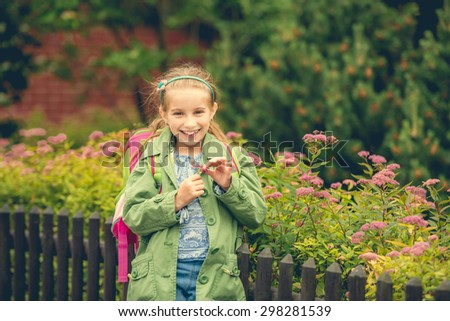 little cute schoolgirl with a school backpack on the background of flowers on the street