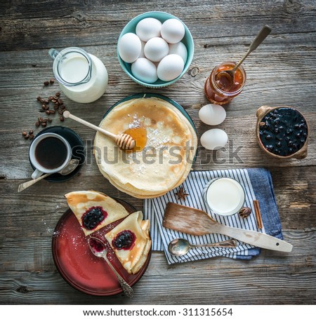 prepared pancakes and coffee among ingredients on wooden background