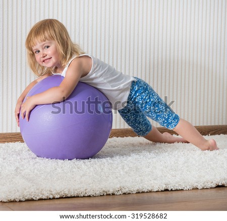 3-year-old  smiling girl with african braids on the ball for fittnesa at home