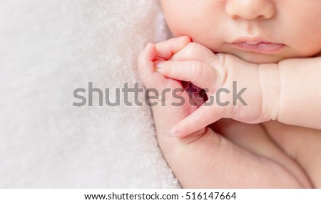 tender lips and nose and crossed fingers of a newborn baby asleep on a diaper, closeup