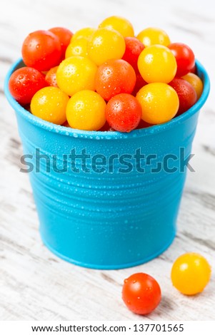 Red and yellow fresh cherry tomatoes with water drops in blue bucket on wooden table