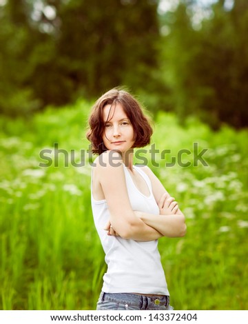 Beautiful freckled young woman with folded arms standing in summer field