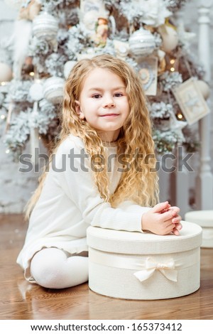Lovely blond little girl sitting under the Christmas tree with gift box