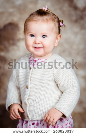 Portrait of beautiful smiling blond little girl with big grey eyes and plump cheeks. Studio portrait on brown grunge background