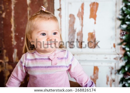 Cute blond little girl with big grey eyes and plump cheeks with pursed lips. Studio portrait on grunge wooden background