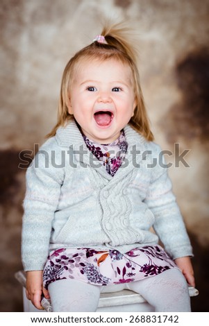 Cute little girl with blond hair sitting on white chair and laughing