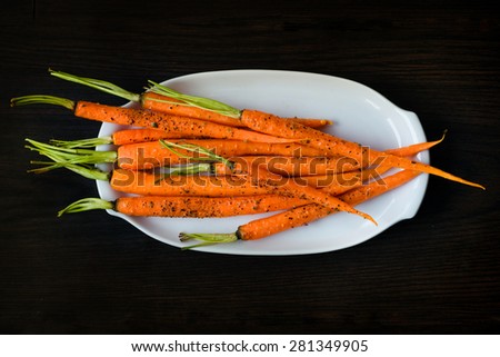 Oven-baked baby carrots sprinkled with fresh-grounded black pepper on white plate on dark table. Healthy vegetarian snack, delicious vegan food