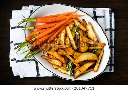 Roasted vegetables seasoned with rosemary and black pepper. Oven-baked baby carrots and potatoes in white bowl on dark table. Healthy vegetarian snack, delicious vegan food