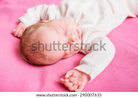Sweet little baby with closed eyes wearing knitted white clothes lying on pink plaid. 2 week old baby sleeping on pink sofa. Security and childcare concept