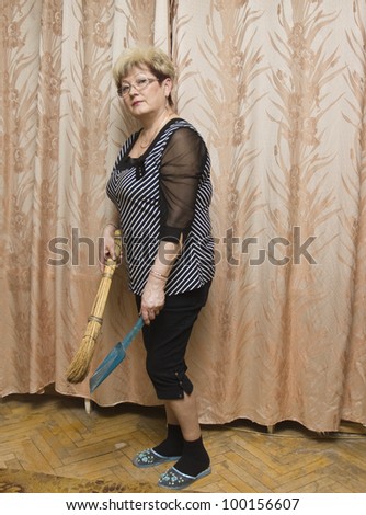 Blond European woman cleaning floor at home with broom and dust pan.