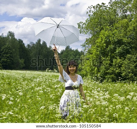 Young woman, brunette, Caucasian, in white dress with white umbrella on a meadow in blossom with white flowers.