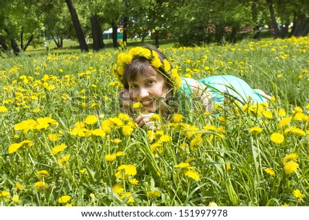 European lady brunette in wreath of yellow dandelions laying on meadow with dandelions.