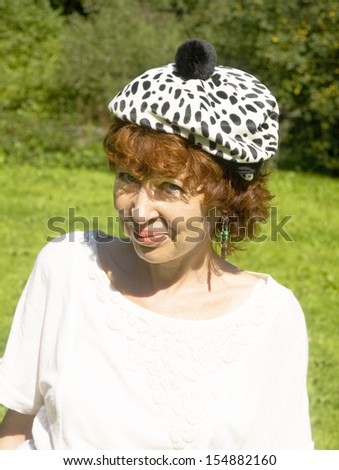 Portrait of European woman with brown hair in white hat with black spots, half body.