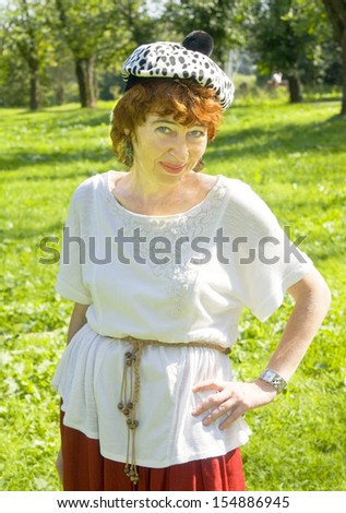 Portrait of European woman with brown hair in white hat with black spots, half body, in park.