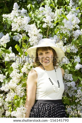 Pretty woman European in white summer hat near shrub with white lilac flowers half body.