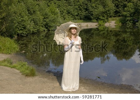 Woman in historical dress of XIX century with white umbrella in park on bank of lake.