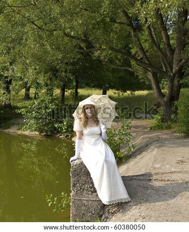 Young woman in white historical dress with white umbrella sitting in park near lake.