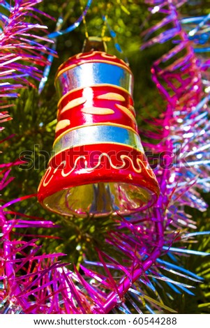 Christmas decoration - bell with silver and red lines on fir tree and garlands.