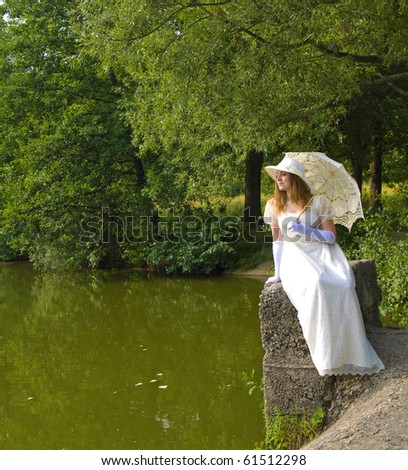 Young lady in white historical dress, white hat with white umbrella sitting near lake in park.