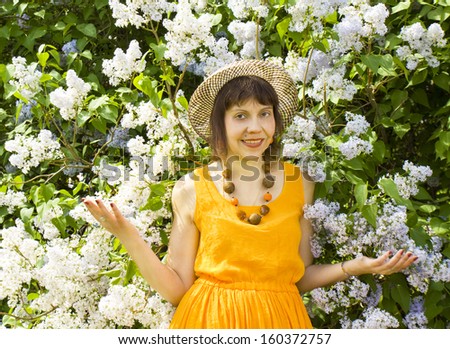 European lady in hat and orange dress near lilac flowers.