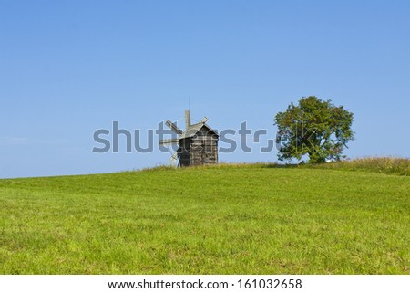 Landscape with windmill and tree on field, recorded in outdoors museum of wooden architecture on island Kizhi on Onega (Onezhskoye) lake in region Karelia in Russia, UNESCO World Heritage site.