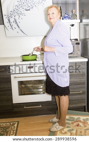 Elderly European blond lady cooking on kitchen near kitchen oven.