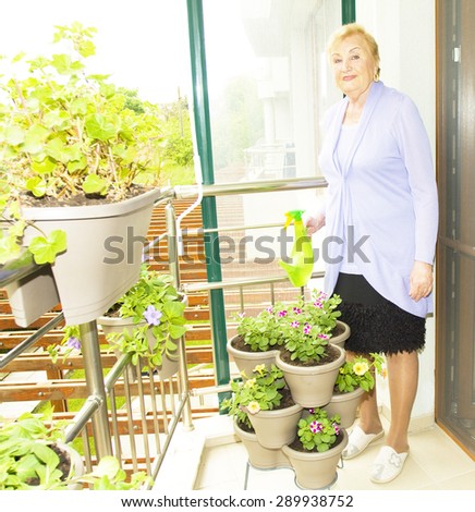 Elderly European blond lady watering flowers with watering pot on balcony.