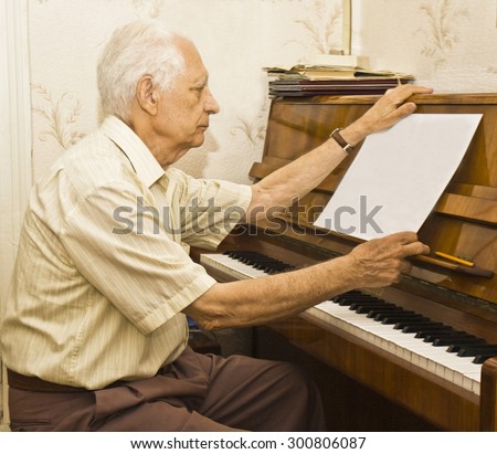 Old man sitting at piano looking at notes.
