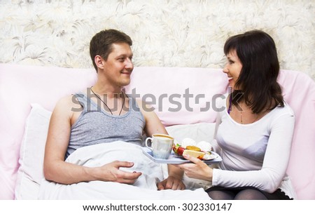 Young woman European brings young man European breakfast in bed.