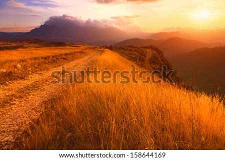 Dirt road and mountain grass towards the sun