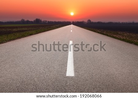 Driving on an empty asphalt road towards the setting sun