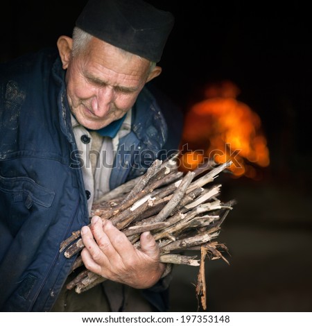 Elderly, poor man carrying firewood for old brick stove