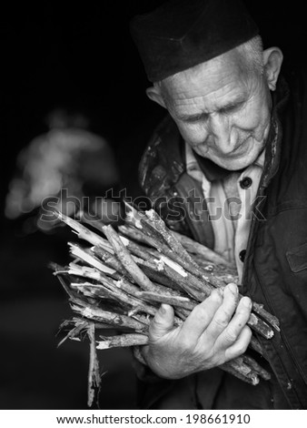 Elderly, poor man carrying firewood for old brick stove