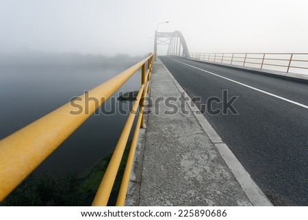 Driving on an empty road over the bridge at foggy morning