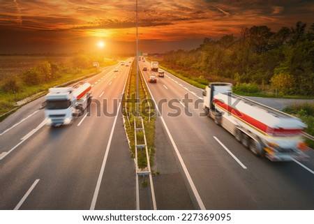 Two white trucks - cisterns in motion blur on the highway at sunset