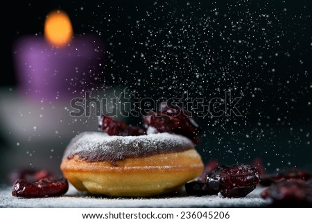 Sprinkling sugar on delicious donut topped with chocolate and cranberries. Romantic atmosphere, candle in background. Shallow depth of field.