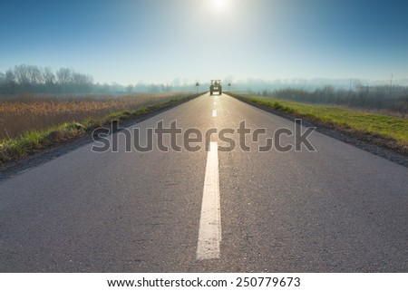 Driving on asphalt road towards the rising sun and upcoming tractor.