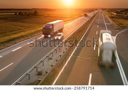 Trucks and car in motion blur on the freeway towards the setting sun. Rush hour on the motorway near Belgrade - Serbia.